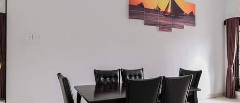 A dining area with a table and chairs, a painting on the wall, and a curtain.