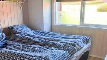 A single bed with a checkered bedspread in a room with wooden walls and a window.