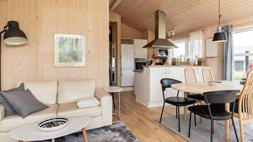 A modern interior with a sofa, a dining table with chairs, a kitchen area, and a large window.