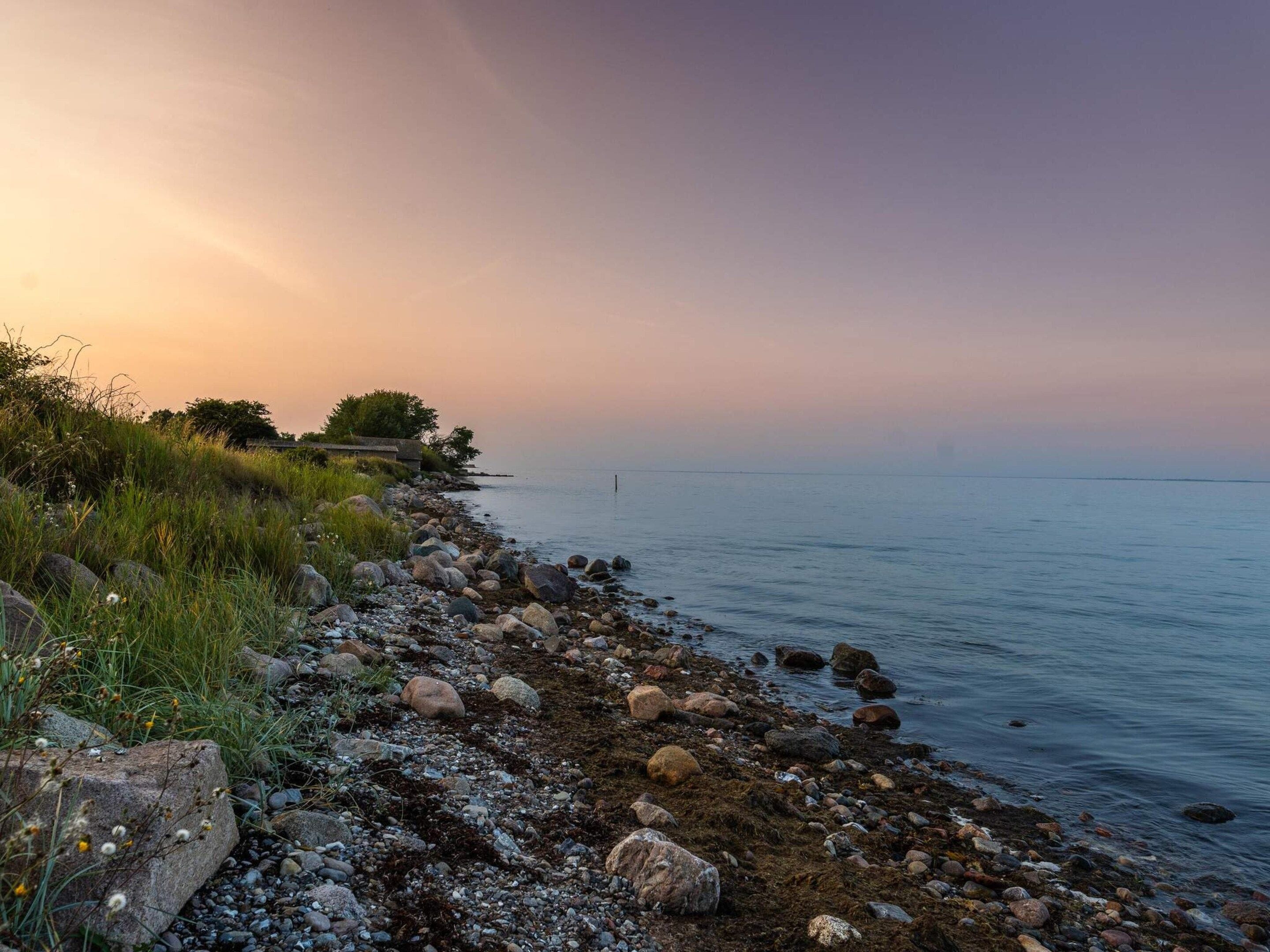 A rocky shoreline with a calm sea and a sunset sky.