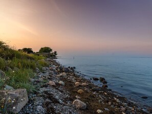 A rocky shoreline with a calm sea and a sunset sky. - 6 Person Holiday Home in Tranekaer (Tranekaer)