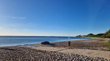 Ein Strand mit Kiesufer, einer Holzpromenade und Booten im Wasser.