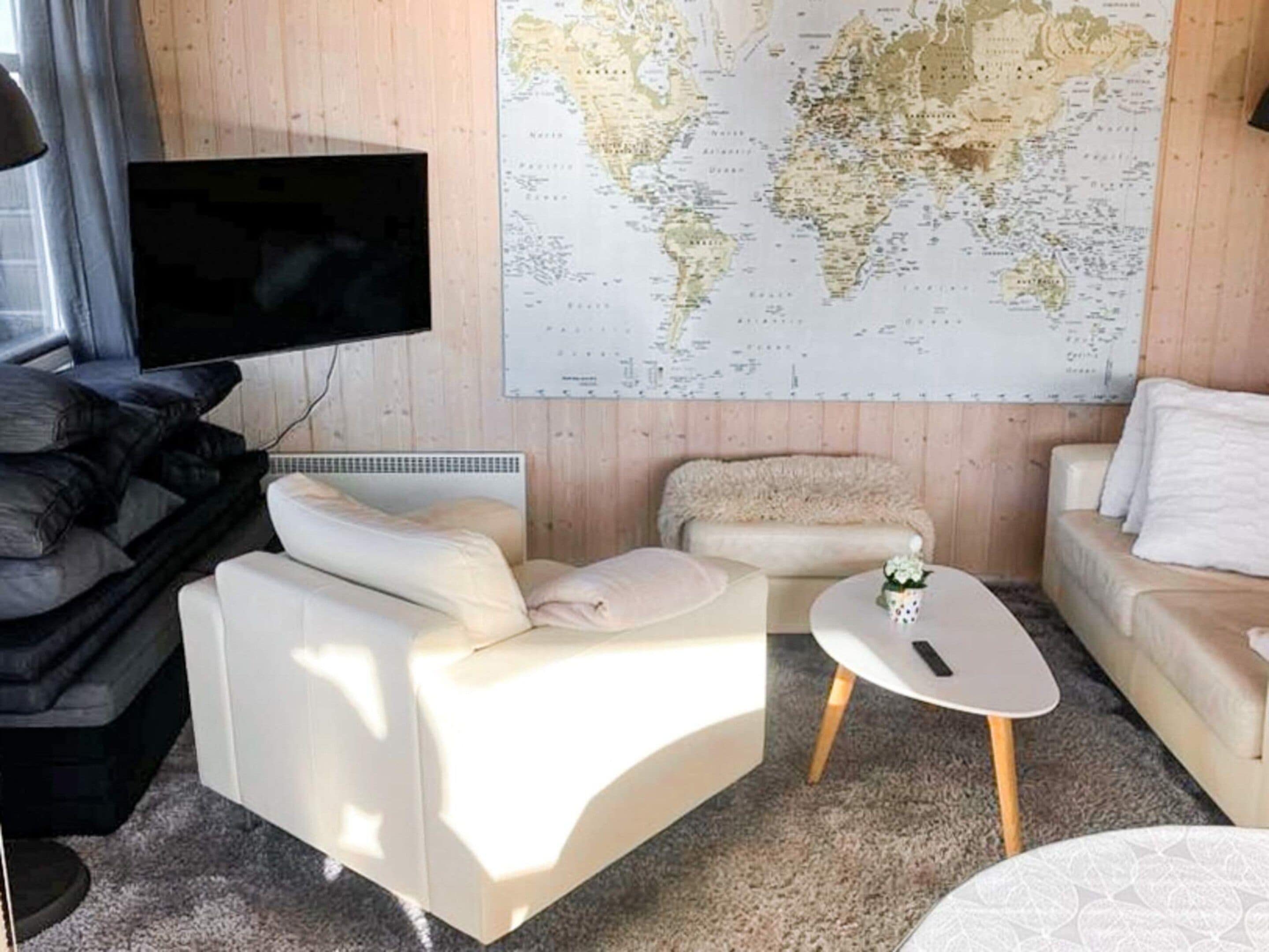 A modern living room with a large world map on the wall, a flat-screen TV mounted above a sofa, and a small round table with a remote control.