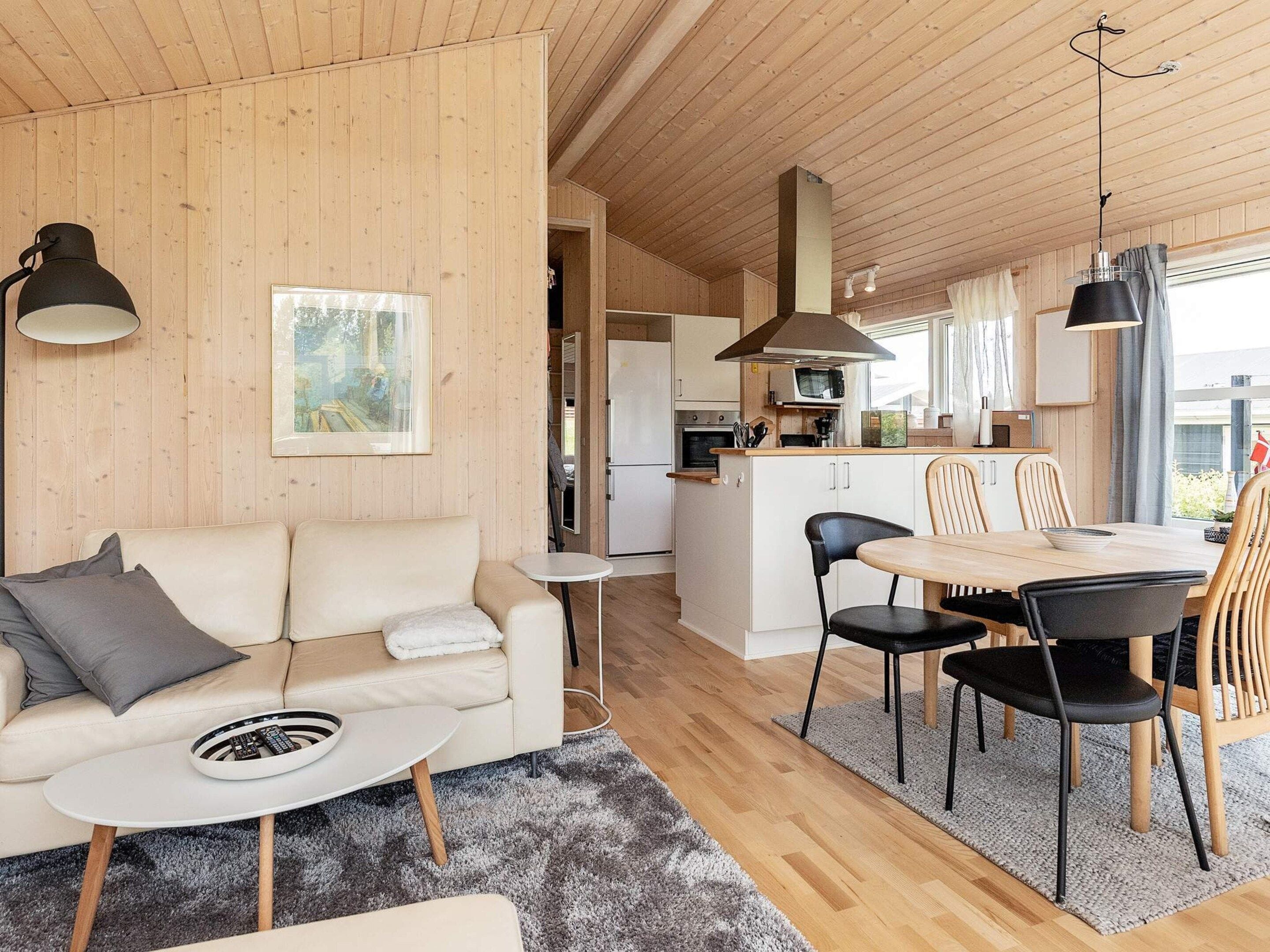 A modern interior with a sofa, coffee table, dining table, chairs, and a kitchen area.