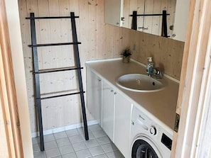 A compact bathroom with a wooden vanity, a sink, a mirror, a washing machine, and a black metal ladder. - 6 Person Holiday Home in Tranekaer (Tranekaer)