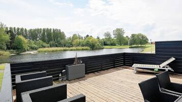 A wooden deck with wicker furniture, a view of a lake, and a grassy area with trees.