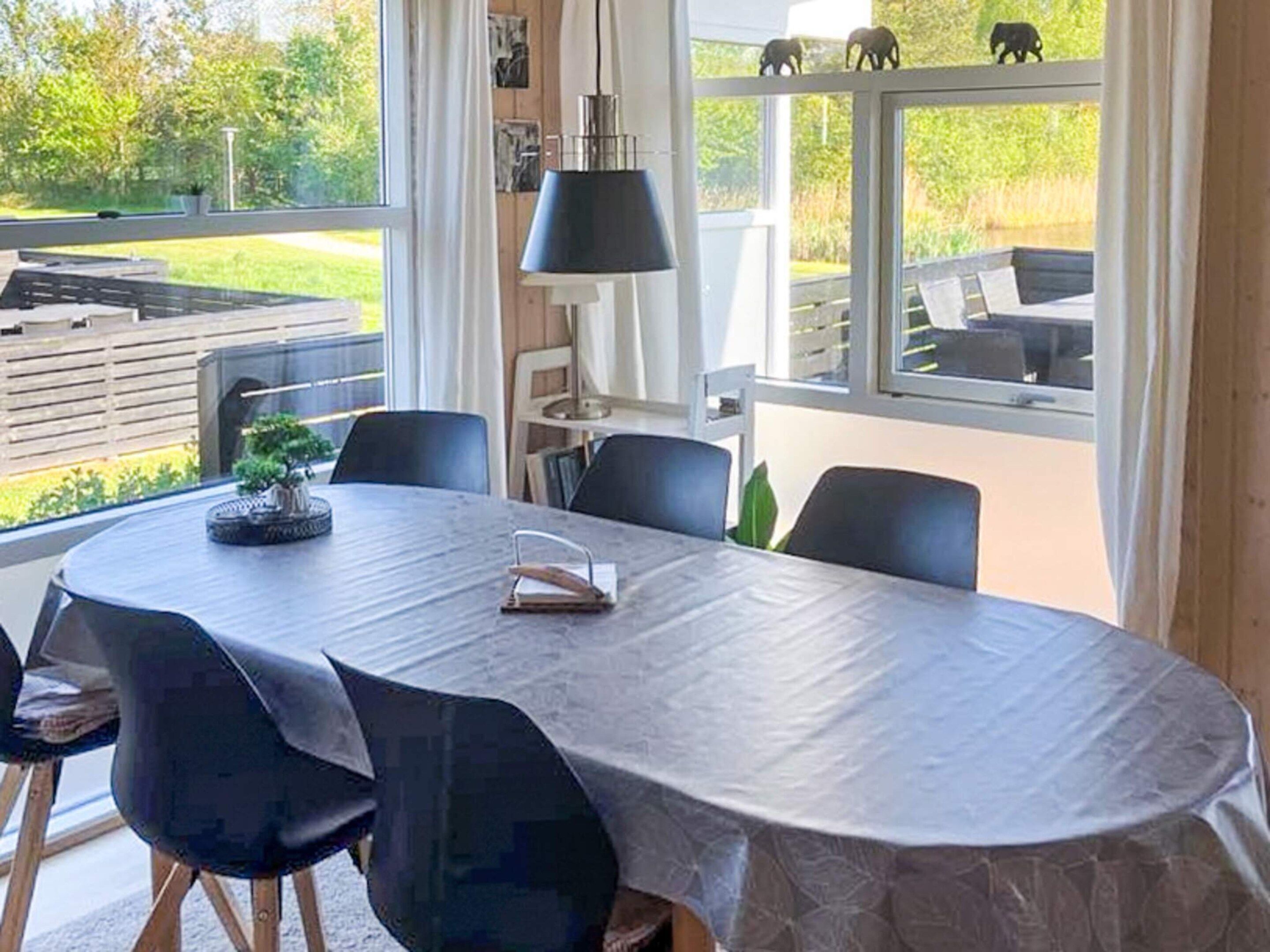 Un coin repas avec une table ronde, des chaises noires, une plante en pot et une vue sur un jardin grâce à de grandes fenêtres.