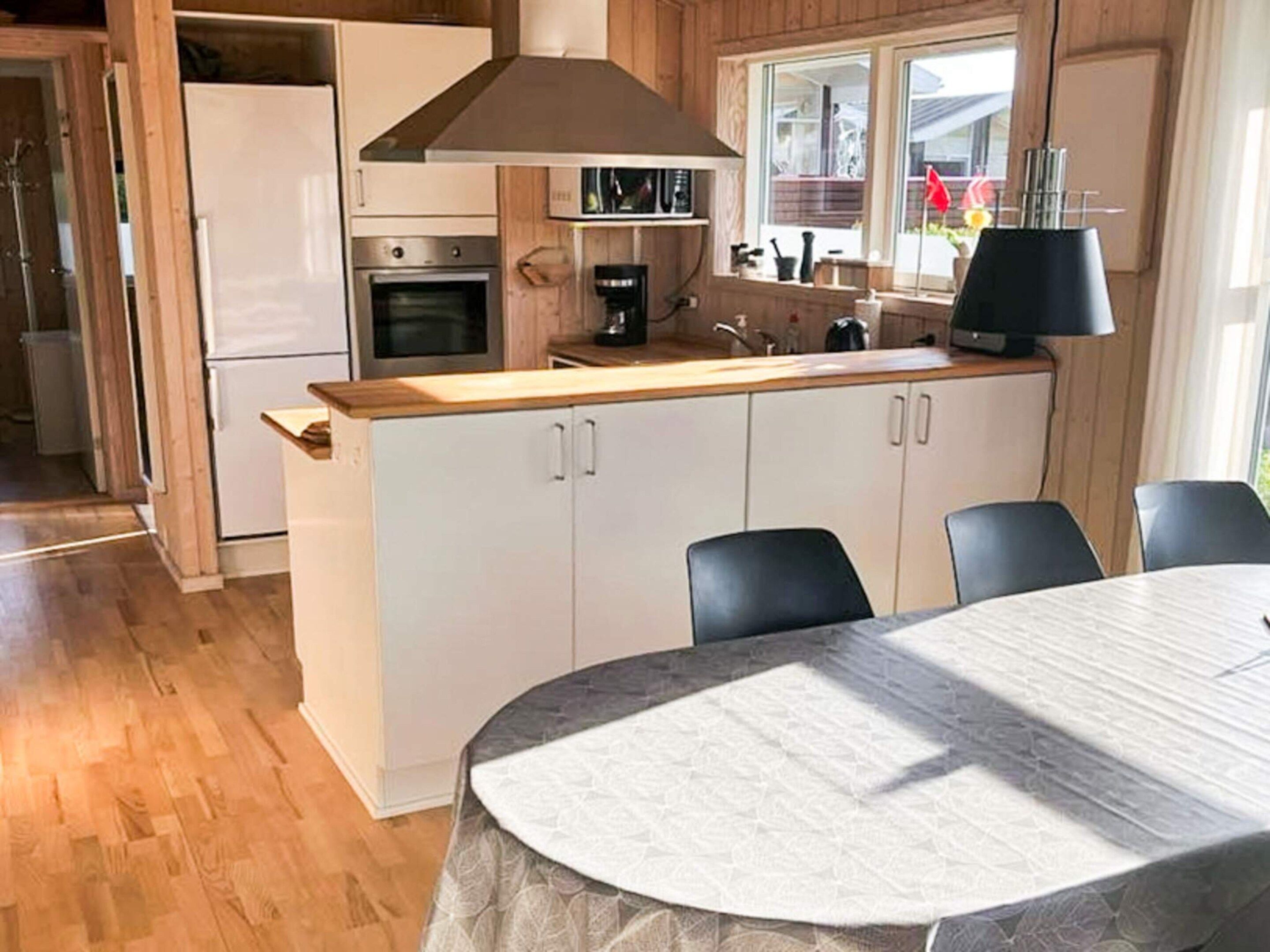 Eine moderne Küche mit weißen Schränken, einer Holz Arbeitsplatte und einem eingebauten Backofen. Im Vordergrund steht ein Esstisch mit Stühlen.
