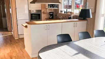 Eine moderne Küche mit weißen Schränken, einer Holz Arbeitsplatte und einem eingebauten Backofen. Im Vordergrund steht ein Esstisch mit Stühlen.