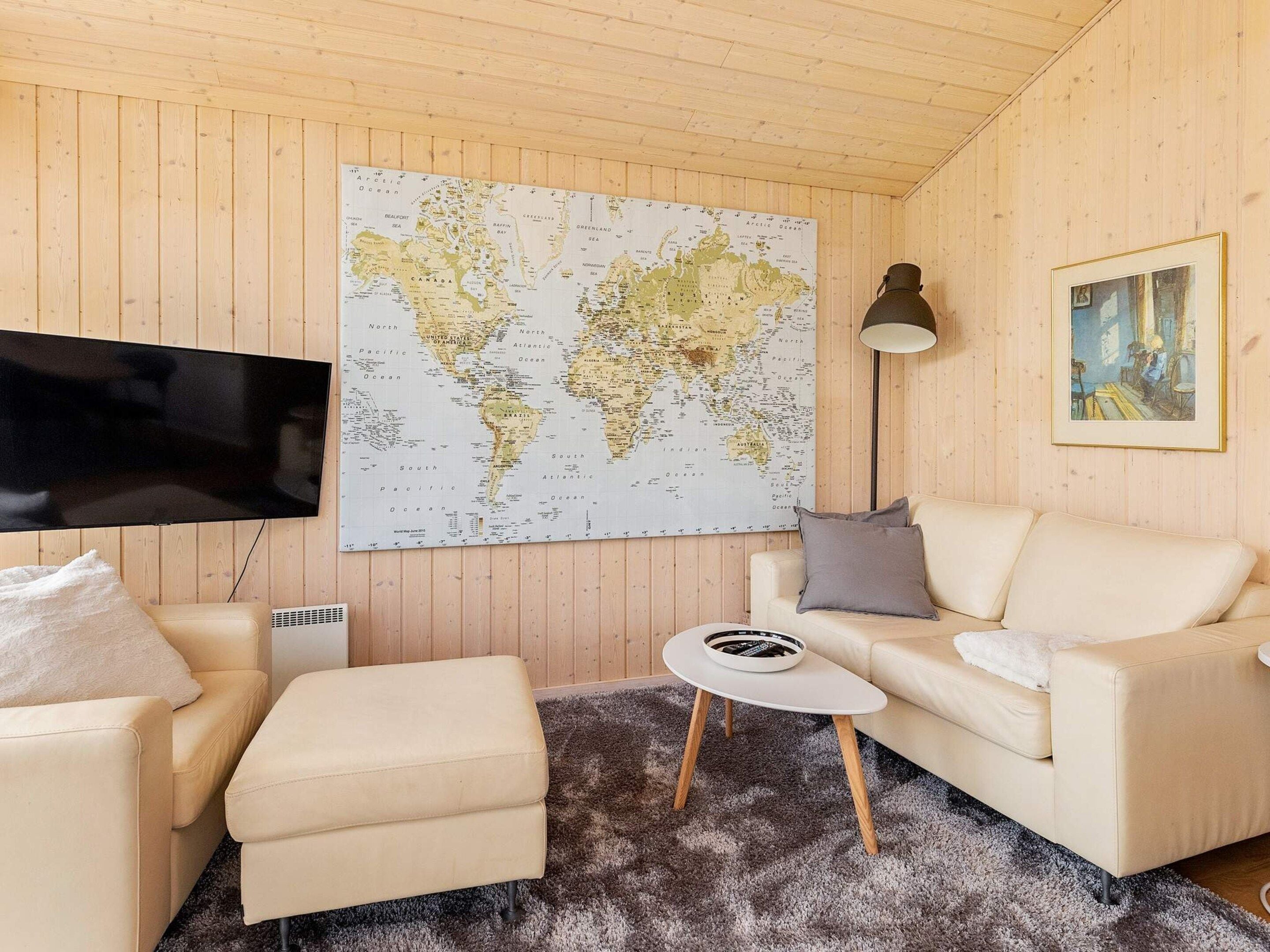 Ein Zimmer mit einer großen Weltkarte an der Wand, einem Fernseher, einem Sofa, einem kleinen Tisch und einer Lampe.