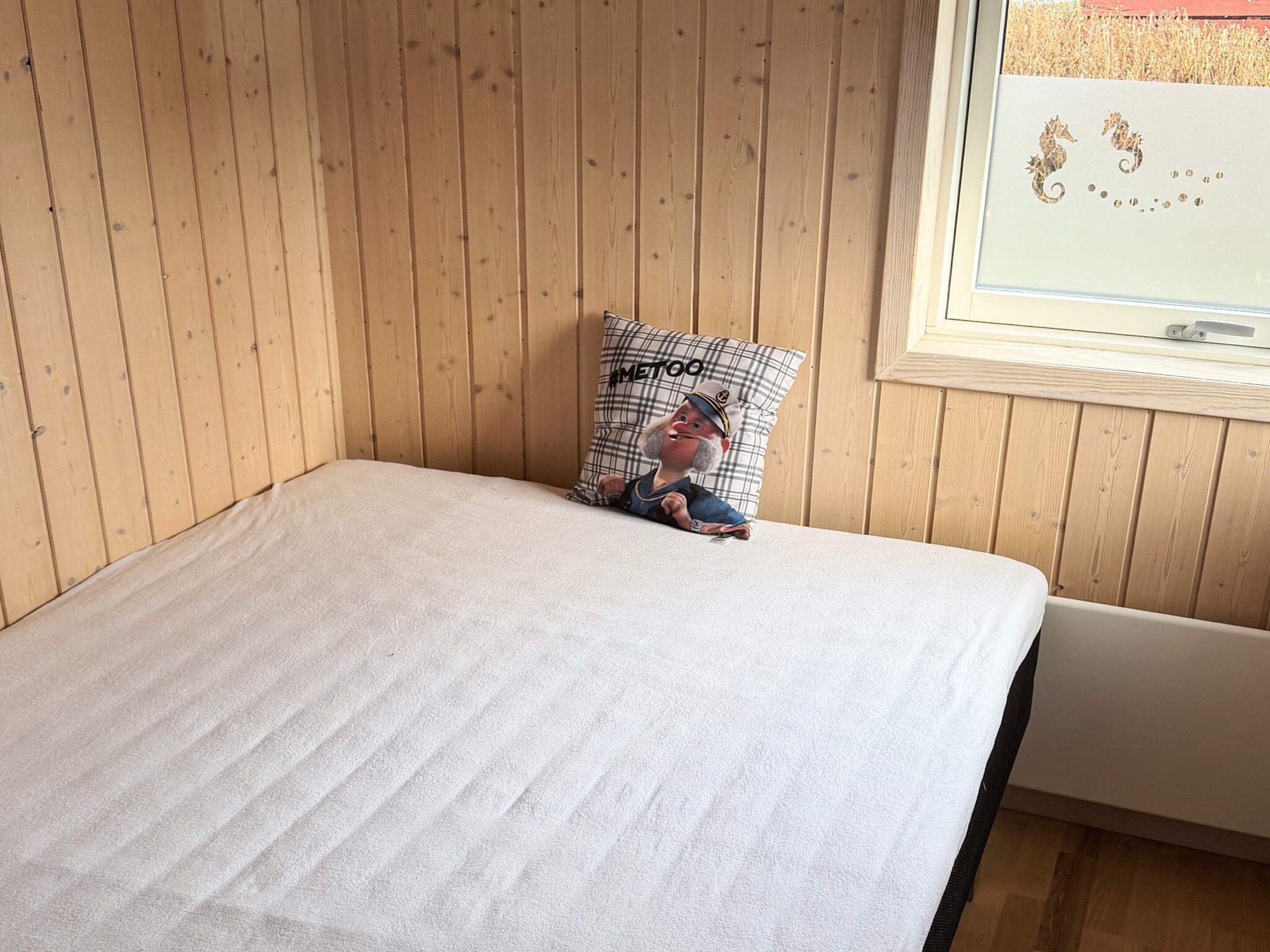 Ein Einzelbett mit weißer Bettdecke in einem Zimmer mit Holzwänden und einem Fenster.
