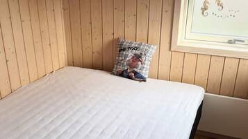 Ein Einzelbett mit weißer Bettdecke in einem Zimmer mit Holzwänden und einem Fenster.