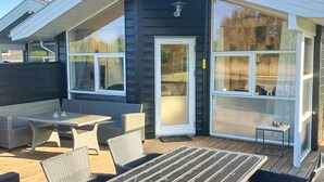 Et moderne hus med mørk facade, store vinduer og en overdækket terrasse med udendørs møbler.