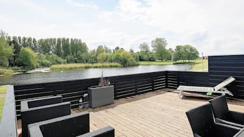 A deck with wicker furniture, a small table, and a view of a lake and trees.