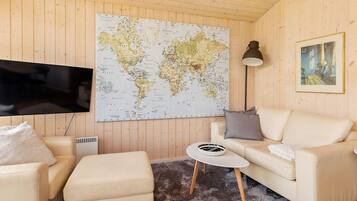 Ein gemütliches Zimmer mit einer großen Weltkarte an der Wand, einem Flachbildfernseher, einem Sofa, einem kleinen runden Tisch und einer Lampe.