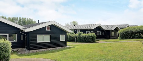 A row of dark-colored mobile homes with a grassy yard and a clear sky.