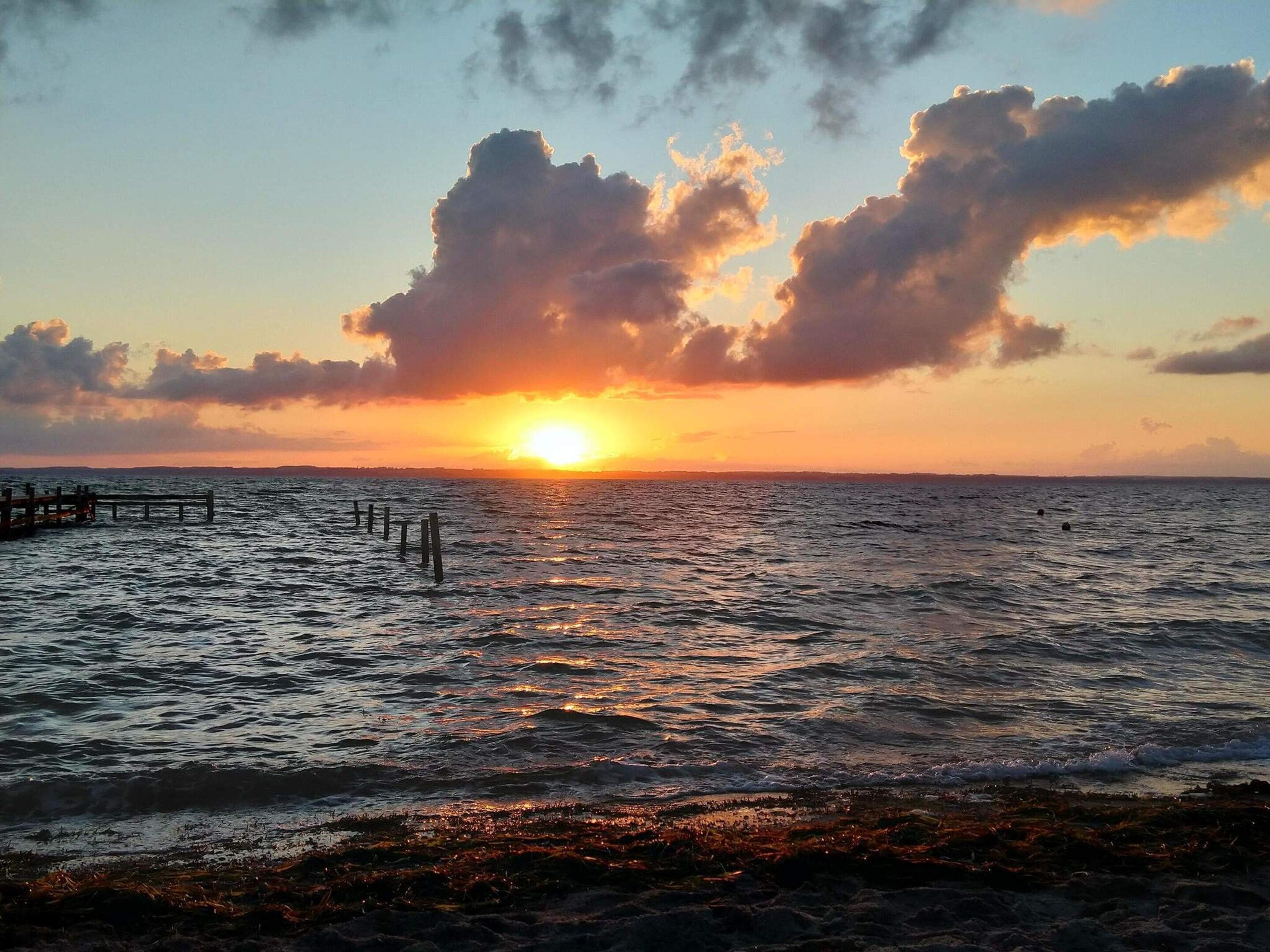 Solnedgang over havet med en træbro, der strækker sig ud i vandet.