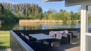 Um deck com móveis de exterior com vista para um lago, rodeado por árvores.