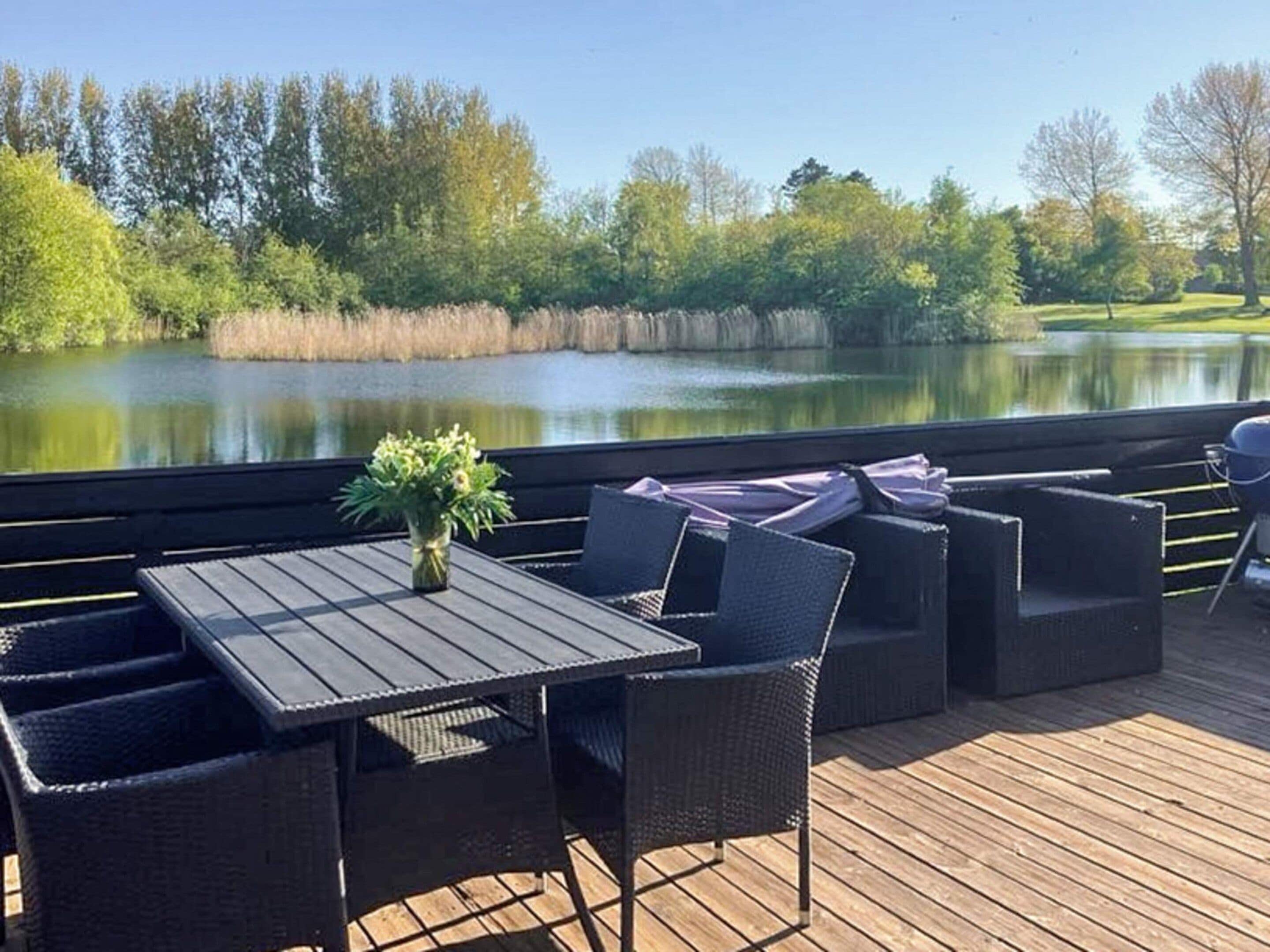 Eine Terrass mit Tisch und Stühlen mit Blick auf einen See, umgeben von Bäumen.