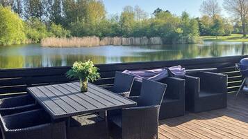 Eine Terrass mit Tisch und Stühlen mit Blick auf einen See, umgeben von Bäumen.