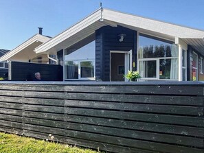 A modern house with a dark exterior, large windows, and a wooden deck in front.
