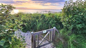 En træport med et skilt, der viser vejen til stranden, omgivet af frodig vegetation og der fører til et vandareal.