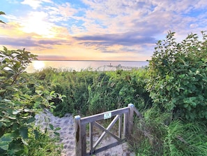 A wooden gate with a sign indicating a beach path, surrounded by lush greenery and leading to a body of water. - 6 Person Holiday Home in Tranekaer (Tranekaer)