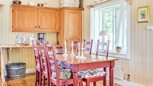 A wooden dining table with chairs, a window with curtains, and wooden cabinets. - 3 Person Holiday Home in Flen (Flen)