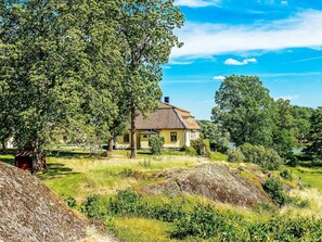 Une maison avec un toit en tuiles, entourée d’arbres et bordée d’un terrain herbeux.