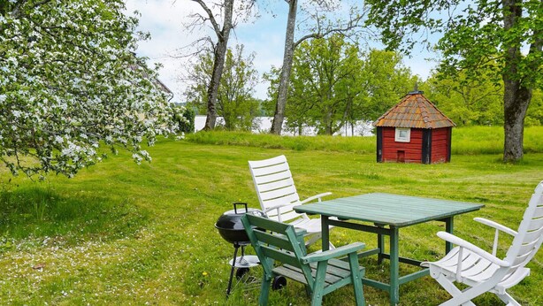 A grassy outdoor area with a table and chairs, a red building, and trees. - 3 Person Holiday Home in Flen (Flen)