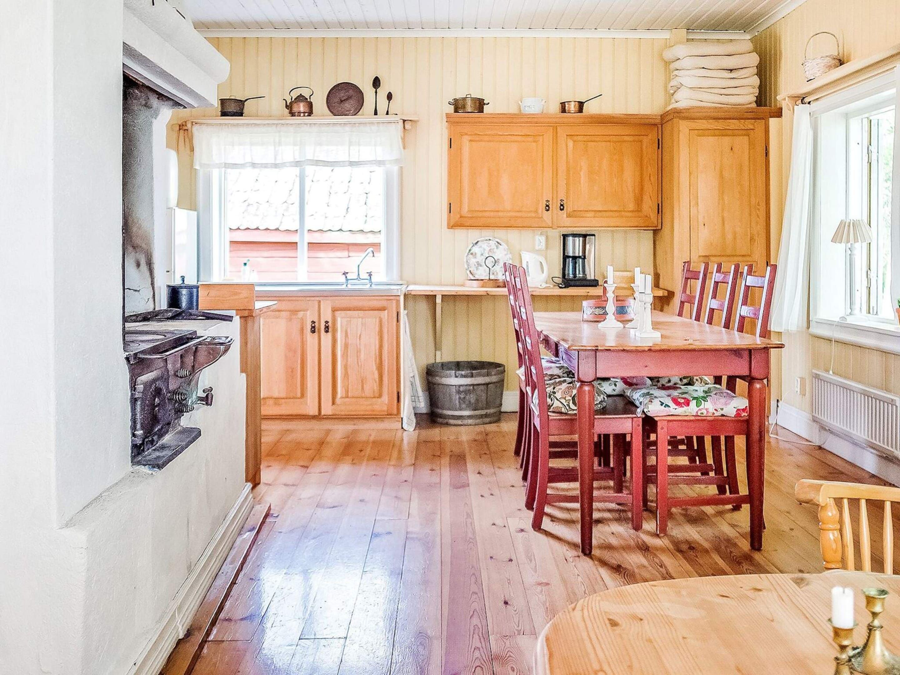 A kitchen with wooden cabinets, a dining table with chairs, a sink, and a window with curtains.