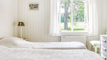 Un dormitorio con dos camas, una ventana con cortinas, un radiador, una lámpara de noche y una mesita.