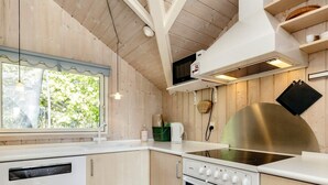 A modern kitchen with wooden walls, a built-in dishwasher, a stove, and a window with a view of greenery. - 6 Person Holiday Home in Vaeggerlose (Vaeggerlose)