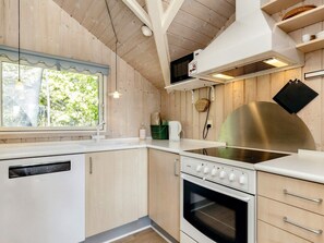 A modern kitchen with wooden walls, a built-in dishwasher, a stove, and a window with a view of greenery. - 6 Person Holiday Home in Vaeggerlose (Vaeggerlose)