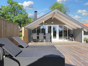 A modern outdoor patio with a covered seating area, a barbecue grill, and a wooden deck. - 6 Person Holiday Home in Vaeggerlose (Vaeggerlose)
