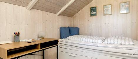 Une pièce avec un plafond en pente, un lit avec une literie blanche, un bureau avec une lampe et des tableaux accrochés au mur.