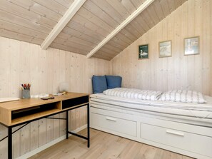 A room with a sloped ceiling, a bed with white bedding, a desk with a lamp, and wall-mounted pictures. - 6 Person Holiday Home in Vaeggerlose (Vaeggerlose)