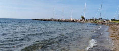 A coastal scene with a rocky breakwater, calm sea, and clear skies.