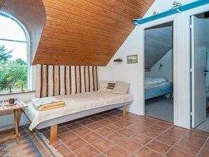 A bedroom with a sloped ceiling, a bed, a small table with a lamp, and a view of another room. - 3 Person Holiday Home in Ringkobing (Ringkobing)
