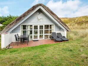A thatched-roof house with a patio, a table, chairs, and two lounge chairs. - 3 Person Holiday Home in Ringkobing (Ringkobing)