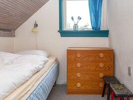 Una camera da letto con un letto, una cassettiera in legno, una finestra con tende e una lampada a muro.