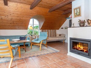 A cozy living room with a fireplace, wooden ceiling beams, and a large window.
