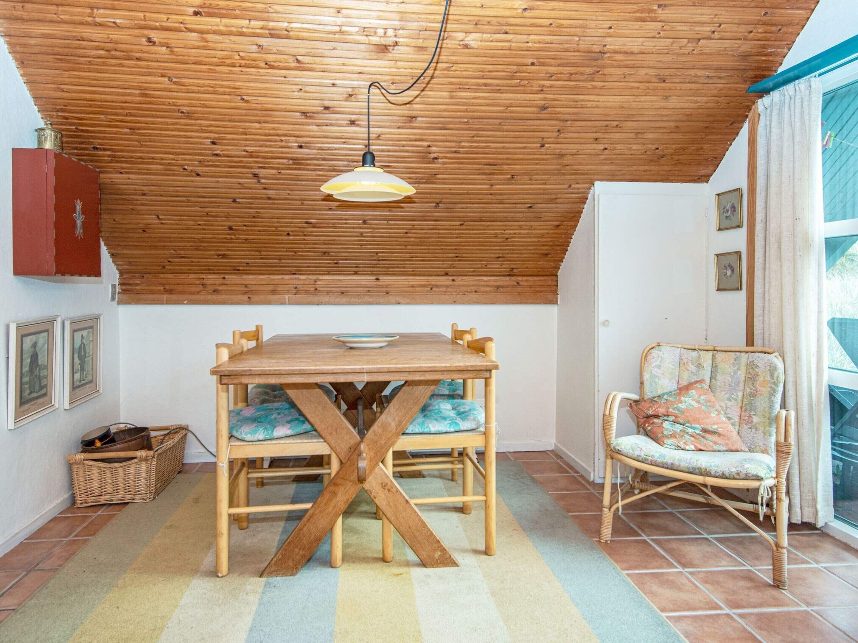 A dining area with a wooden table and chairs, a hanging light fixture, and a wicker chair with a cushion.