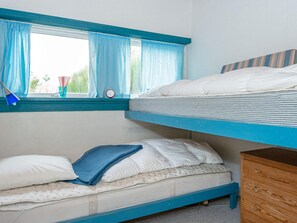 Une chambre avec un lit superposé, une fenêtre, une lampe de chevet et une commode en bois.