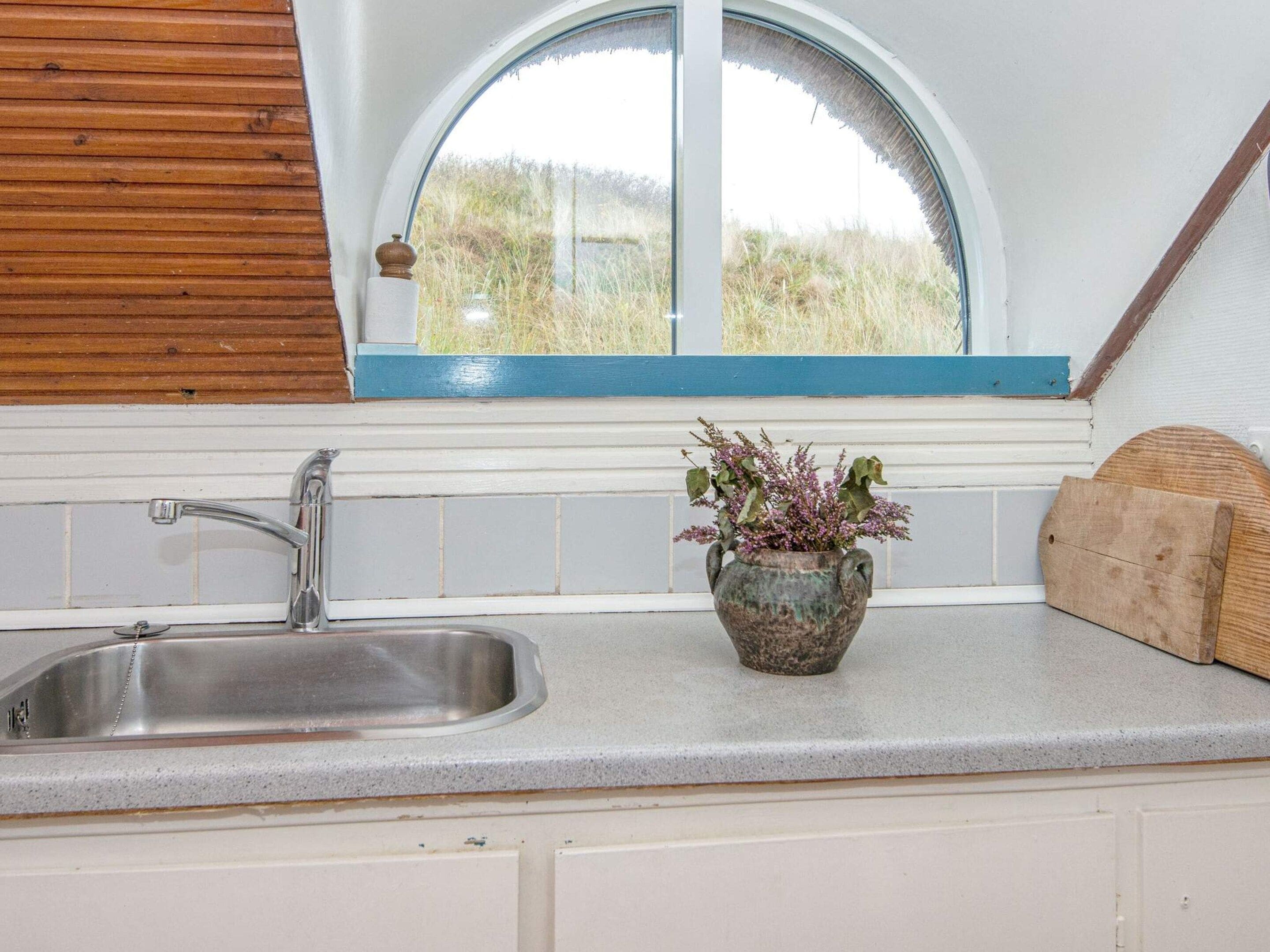 A kitchen with a stainless steel sink, a window with a view of greenery, and a rustic wooden cutting board.