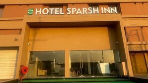 Ein Hotel namens Hotel Sparsh Inn mit einer modernen Fassade, einem großen Glasvordereingang und einer Grünfläche davor.