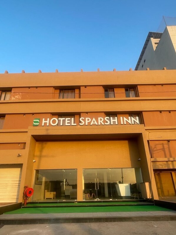 Un hotel llamado 'HOTEL SPARSH INN' con una fachada moderna, amplios ventanales de vidrio y una entrada con alfombra verde.