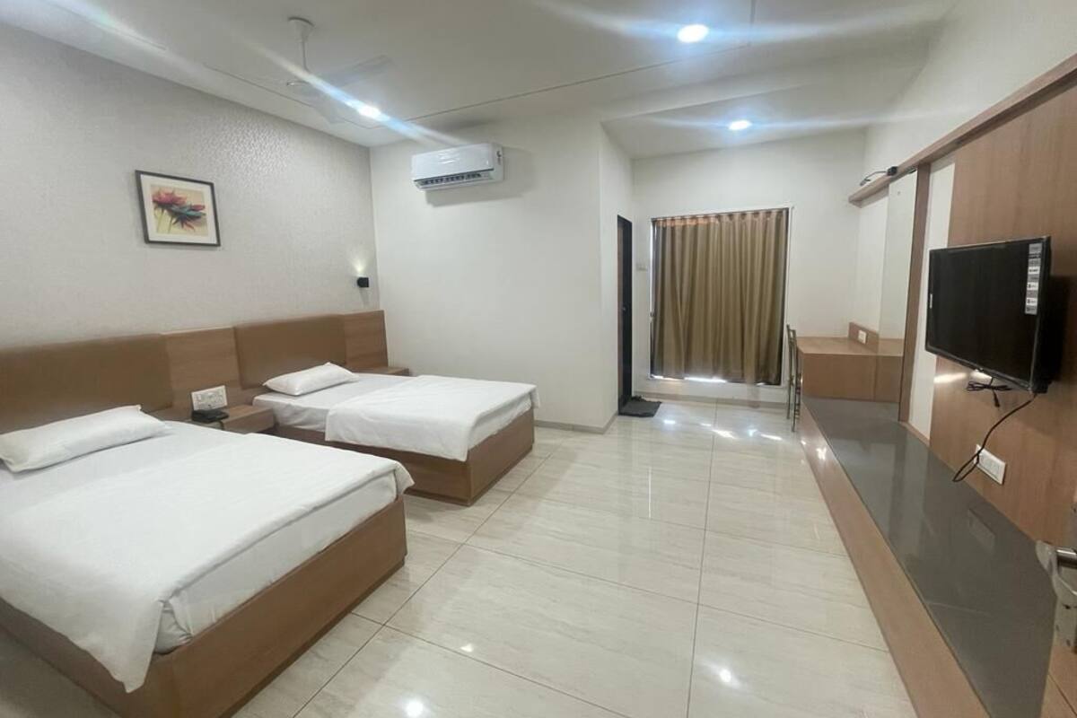 A hotel room with two beds, a television, an air conditioner, and a window with curtains.