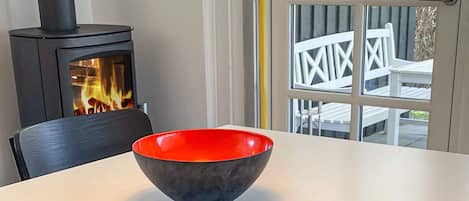 Un intérieur moderne avec un poêle à bois noir, une table blanche et un bol rouge.