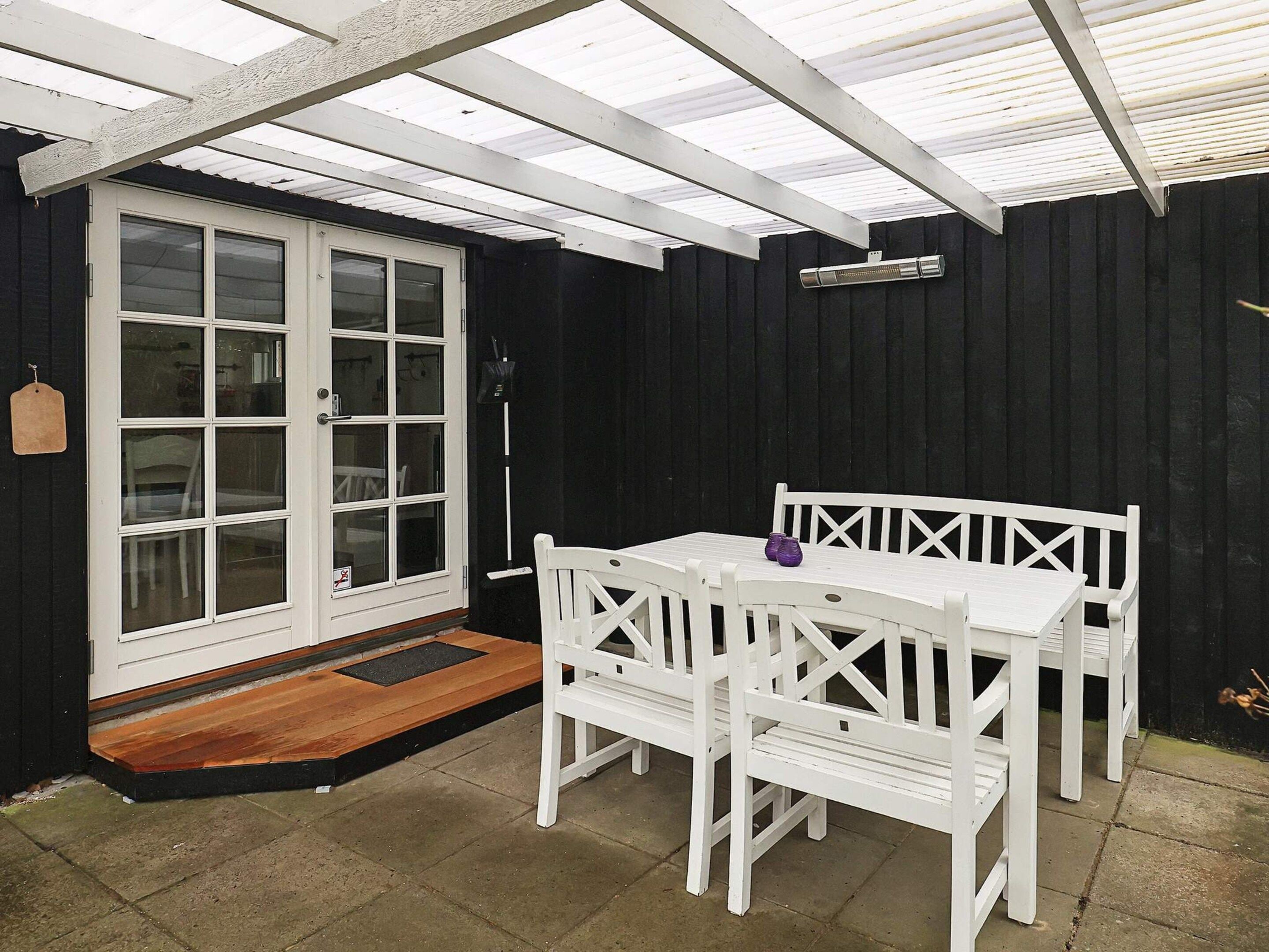 Un patio techado con una mesa y sillas, una puerta con paneles de vidrio y una pared negra.